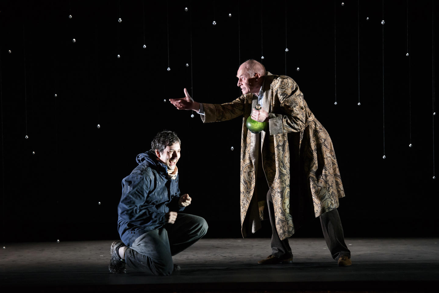 A young man crouches on the floor as Old Man reaches over him clutching a vial of green liquid in The Devil Inside