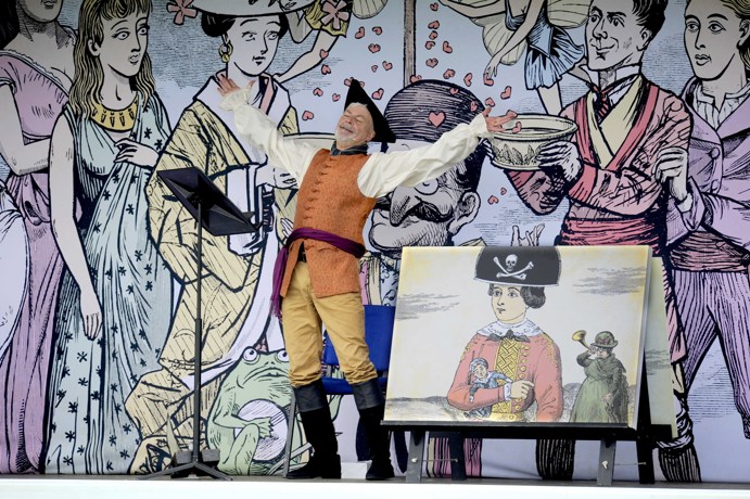 Allan Dunn in Pop-up Opera with his arms outstretched, wearing an orange pirate costume, next to an illustration of a young man wearing a pirate hat