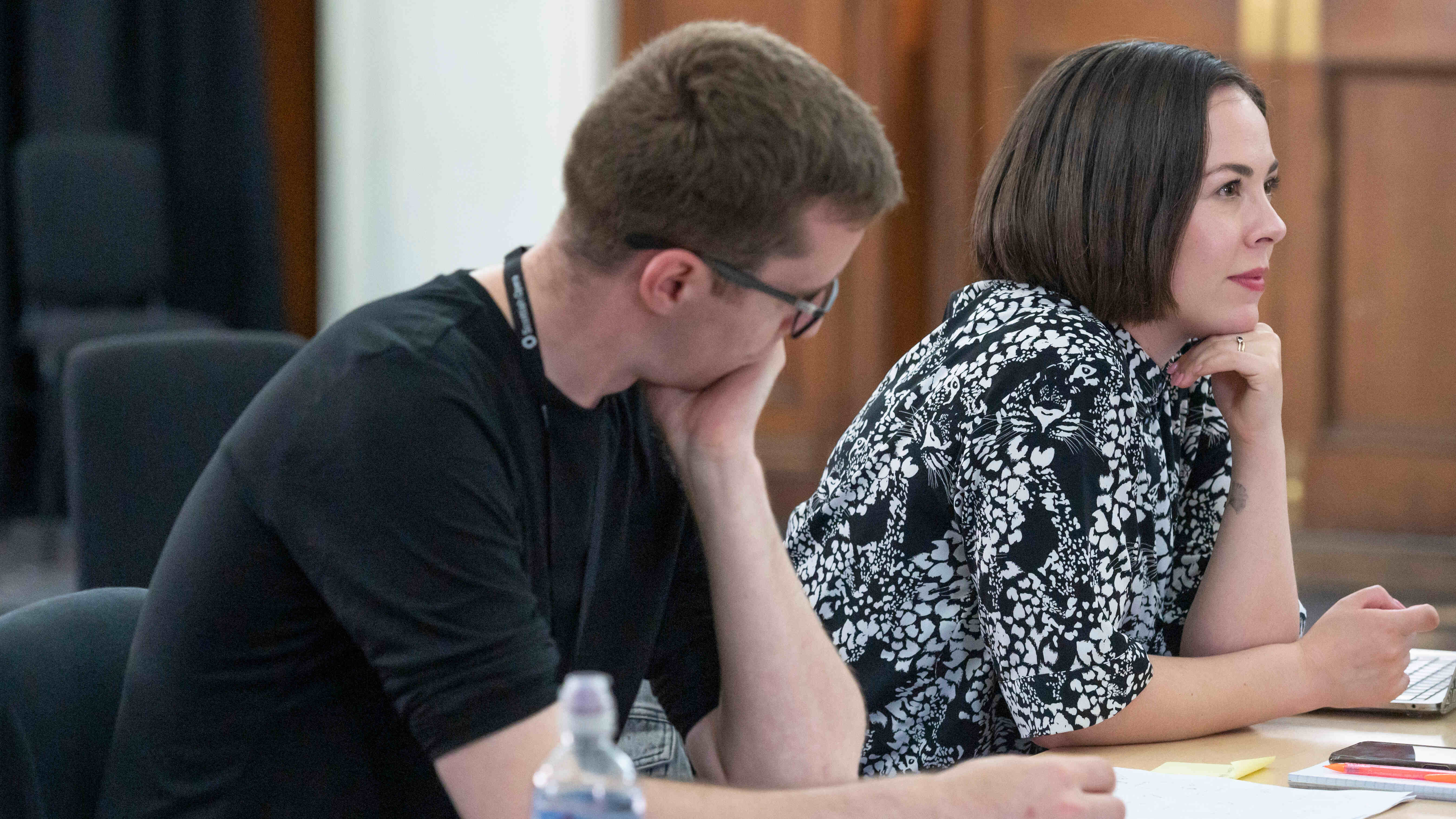 A white man in a black t-shirt and a white woman in a black and white top sitting at a desk.