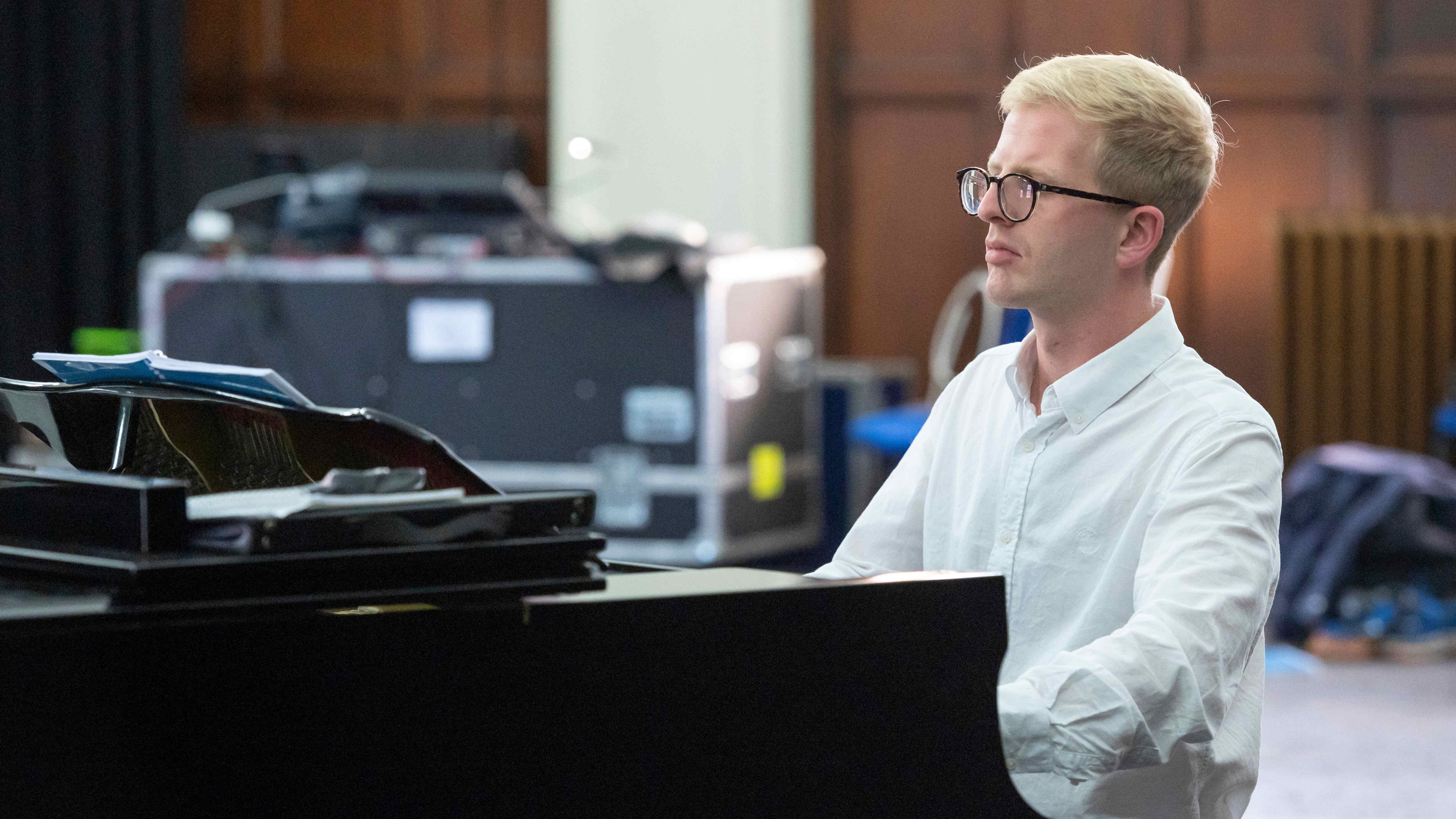 A white, blonde man with glasses plays the piano.